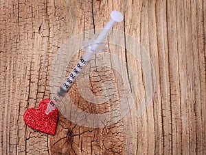 Glitter red heart and syringe with drug over wooden background.