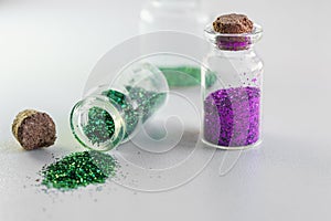 Glitter sales ban in Europe concept. Environmental protection. Purple and green glitter in glass bottles. Isolated on white