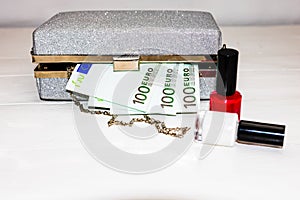Glittery silver clutch bag with money and beauty products isolated on white background with copy space