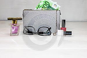 Glittery silver clutch bag with money and beauty products isolated on white background with copy space
