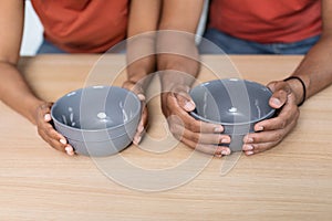 Global crisis and starving. Hands of despaired millennial black wife and husband in t-shirts hold empty plates on table