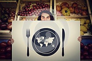 Global hunger, food supply issue. Shocked man holding a warning message banner in front of a grocery store. World map in a plate