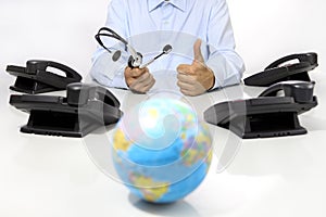 Global international support concept, headset and office phone on desk with globe map