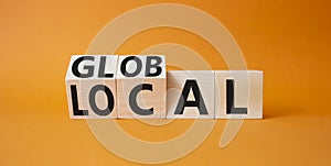 Global and Local symbol. Turned wooden cubes with words Global and Local. Beautiful orange background. Business and Global and