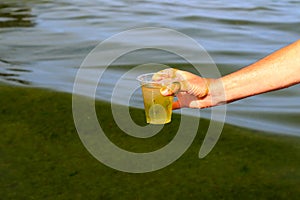 Global pollution of the environment and water. A man collects dirty green water with algae into a glass. Water bloom