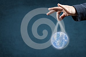 Globalization, Energy and ecology concept. man`s hand in suit holds the planet earth by the strings. blue background, copy space