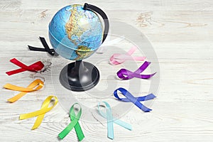 The globe with circle of colorful awareness ribbons on wooden table. World cancer day concept, February 4