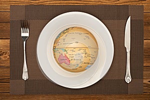 A globe on a dish with fork and knife nearby concept of overusing the resource of nature