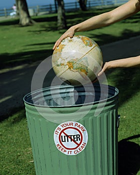 Globe in hands over waste basket,