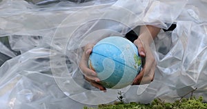 globe in hands plastic film green forest, Pollution of the environment.