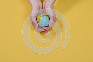 Globe in hands on a yellow background with copy space. The whole world is in your hands. Protect the world from war and disaster