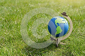 Globe of the planet Earth standing on green grass in sunny day on spring or summer, Eco symbol, Green map on blue globe on lawn in