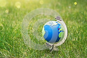 Globe of the planet Earth standing on green grass in sunny day on spring or summer, Eco symbol, red heart and Green map on blue
