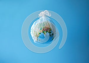 A globe in a plastic bag on a blue background. Concept: plastic garbage turns the planet into a waste dump.