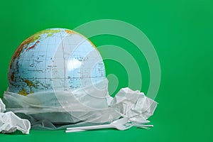Globe in plastic bag and garbage on green background, space for text. Environmental conservation