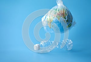 A globe in a plastic bag over a plastic bottle on a blue background. Concept: plastic garbage turns the planet into a waste dump.