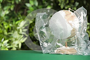 Globe in plastic bag on table against green leaves, space for text. Environmental conservation