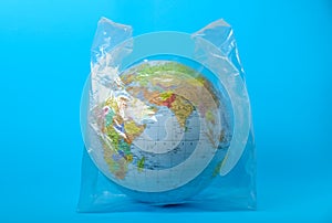 Globe in plastic bag on turquoise background. Environmental conservation