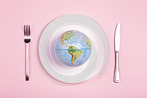 Globe on a plate for food on a pink background. Power, economy, politics, globalism, hunger, poverty and world food concept photo