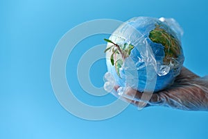 A globe wrapped in plastic wrap, at arm`s length. Sprouts break through the polyethylene. Copy space