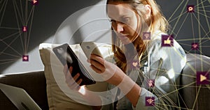 Globes of digital icons spinning caucasian woman using smartphone and digital tablet at home