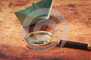 Globetrotter or Journey Explore Concept, Magnifier Glass and Paper Boat Layout on World Map Background, Still-Life Creative Idea., photo