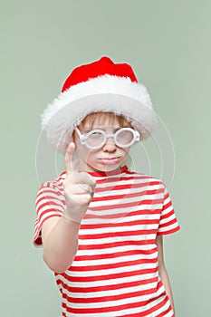 Gloomy Angry boy in a santa hat threatens finger