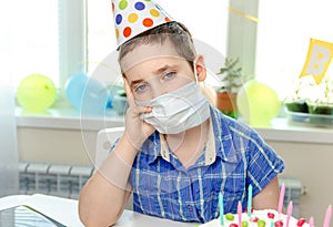 Gloomy child sitting in front of a piece of cake. Birthday party alone