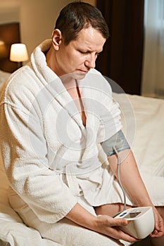 Gloomy male in a bathrobe measures blood pressure with tonometer