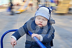 A gloomy pensive little boy rides a merry-go-round on the playground