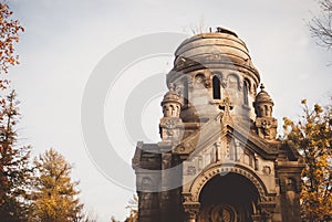 Gloomy statues, monuments, and gravestones of the cemetery on sunny autumn afternoon. Golden yellow twilight covering the trees.