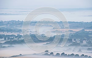 Glorious landscape image of layers of mist rolling over South Downs National Park English countryside during misty Summer sunrise