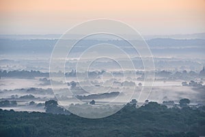 Glorious landscape image of layers of mist rolling over South Downs National Park English countryside during misty Summer sunrise