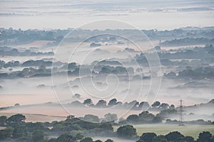 Glorious landscape image of layers of mist rolling over South Downs National Park English countryside during misty Summer sunrise
