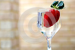 Glossy red strawberry floating in a glass of water