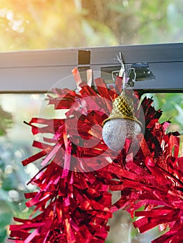 Glossy silver Christmas ball with red ribbon hanging on window. Stylish christmas decorations. Christmas and New Year display for