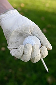 Glove on hand holding golf ball and tee