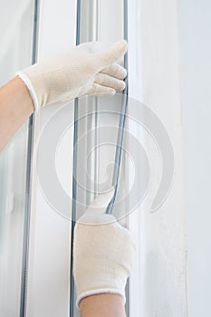 A gloved craftsman lays a rubber seal when installing a new plastic window, close-up