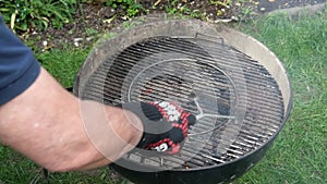Gloved hand Cleaning burnt food on dirty barbecue grill grates with brush