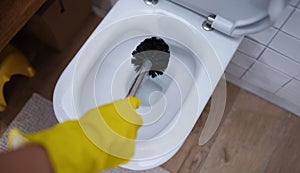 Gloved hand is cleaning toilet with brush closeup