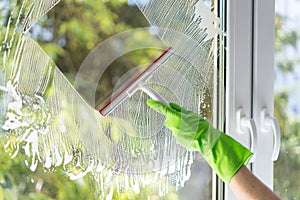 Gloved hand cleaning window with wiper at home