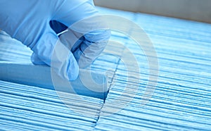 Gloved hand of doctor pulls out disposable blue medical napkin closeup