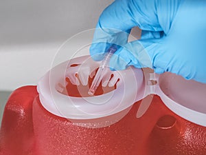 Gloved hand dropping a used needle into a bright red sharps container photo