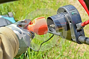 Gloved hand with electric cable and plug connects the lawn mower to the power supply.