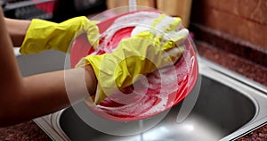 Gloved hand foamy sponge washes red plate closeup