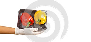 Gloved hand holding packed bell peppers. Red and yellow sweet peppers in plastic food wrap on palm