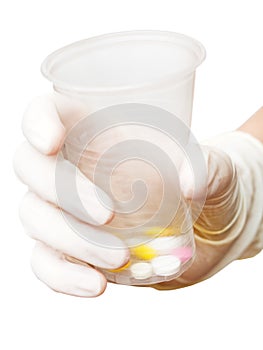 Gloved hand holding plastic cup with pills