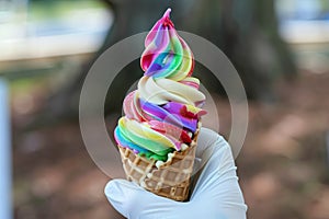 gloved hand holding a rainbow swirl in waffle cone