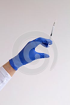 Gloved hand holding a syringe on grey background.