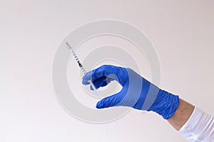 Gloved hand holding a syringe on grey background.